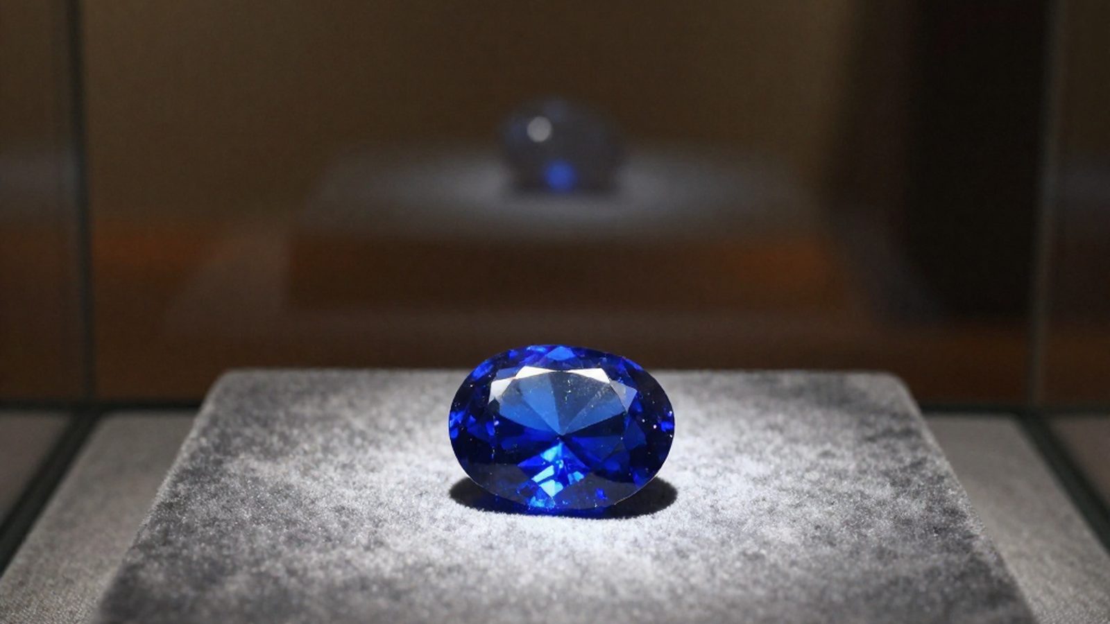 Una gemma blu sfaccettata posata su velluto scuro dentro una teca di vetro, illuminata da un solo fascio di luce dall'alto