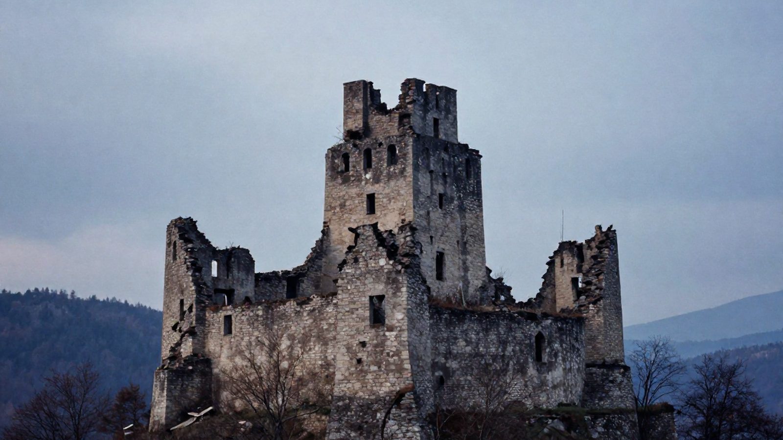 Un castello di pietra in rovina su una collina boscosa dei Carpazi, fra le nuvole basse al crepuscolo