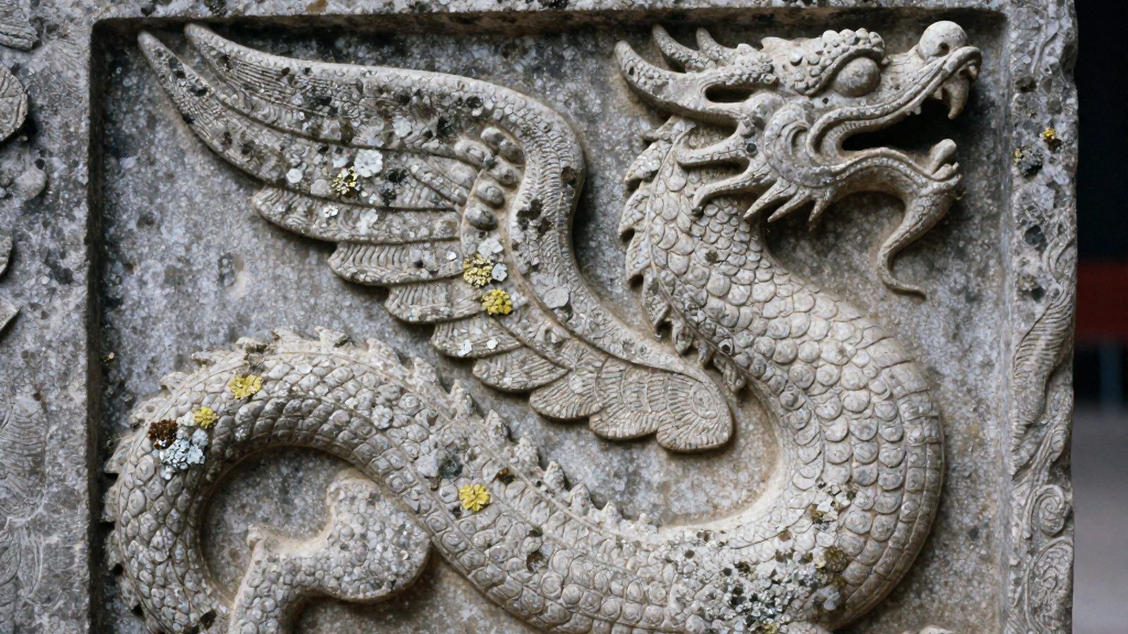 Un bassorilievo di pietra consumato dal tempo, con un drago serpentiforme scolpito su un muro di tempio